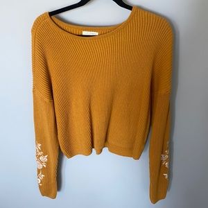 mustard yellow sweater with white flower detail on sleeves